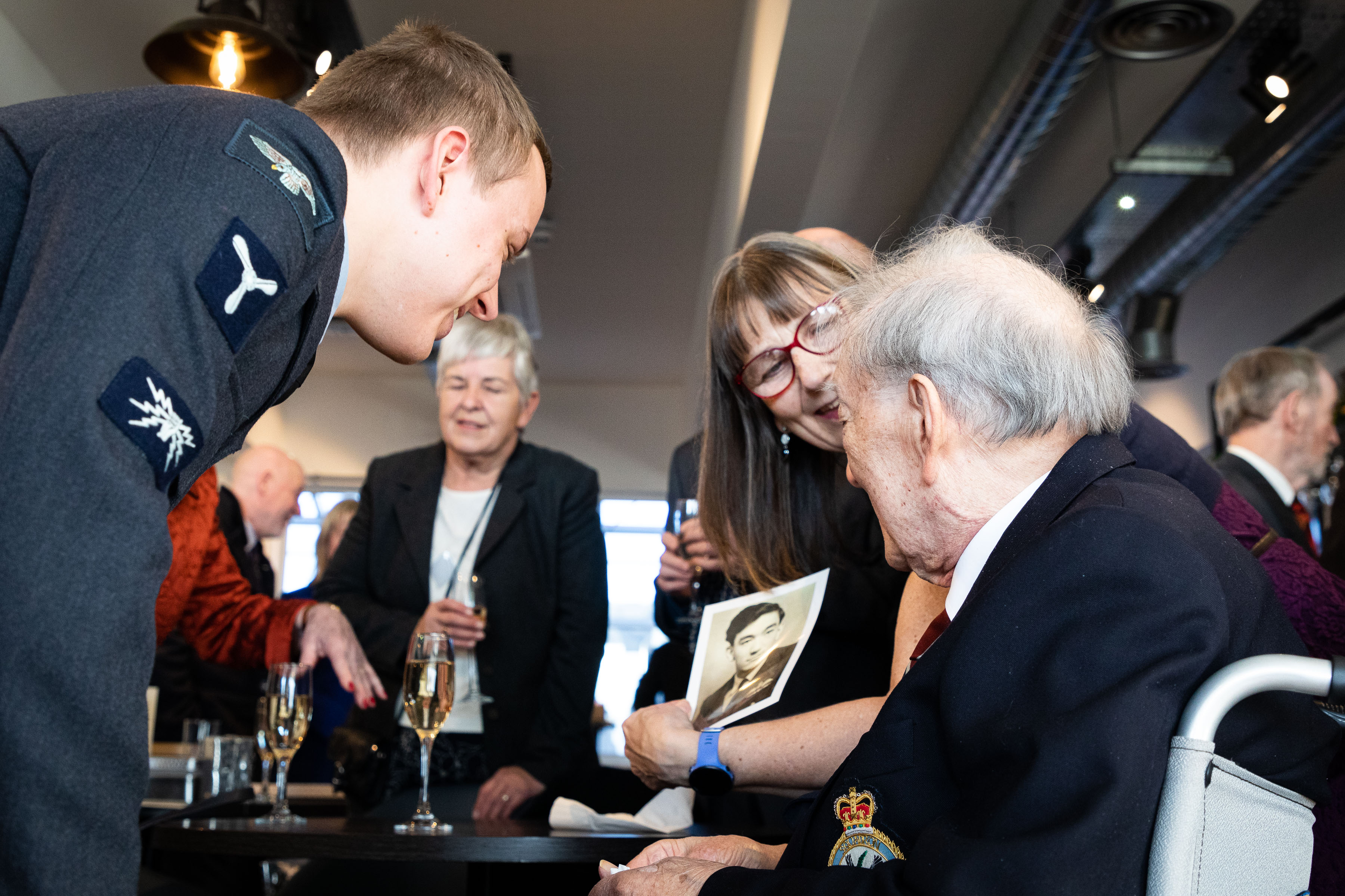 Image shows RAF aviators and veteran looking at black and white picture.